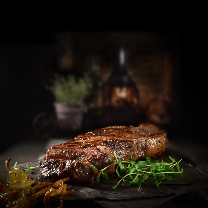 Bone-in Rib-Eye Steak auf eine Schieferplatte umgeben von Kräutern. Gegrillt auf dem Big Green Egg